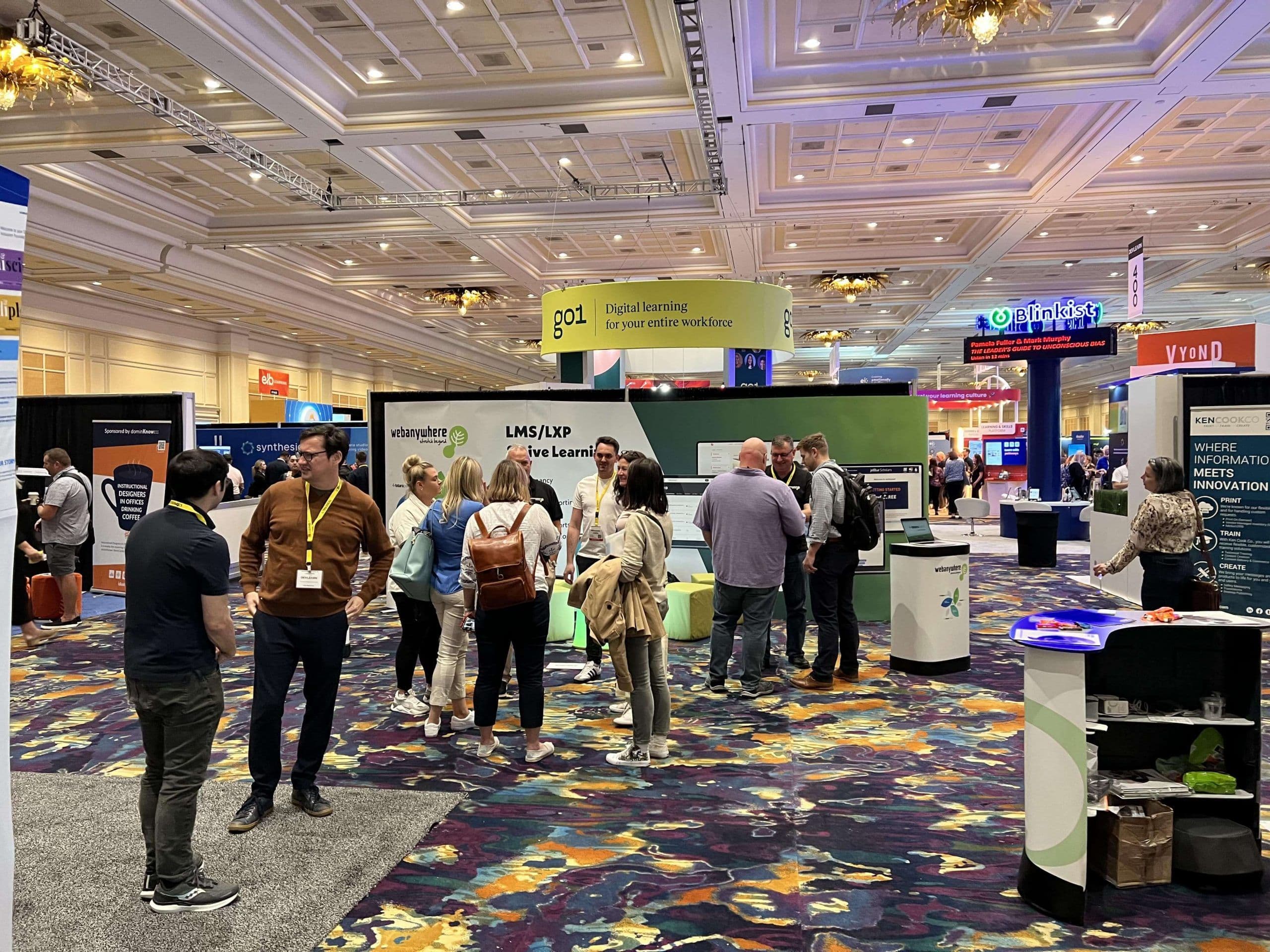 Visitors talk beside the Webanywhere booth on the DevLearn 2022 expo floor