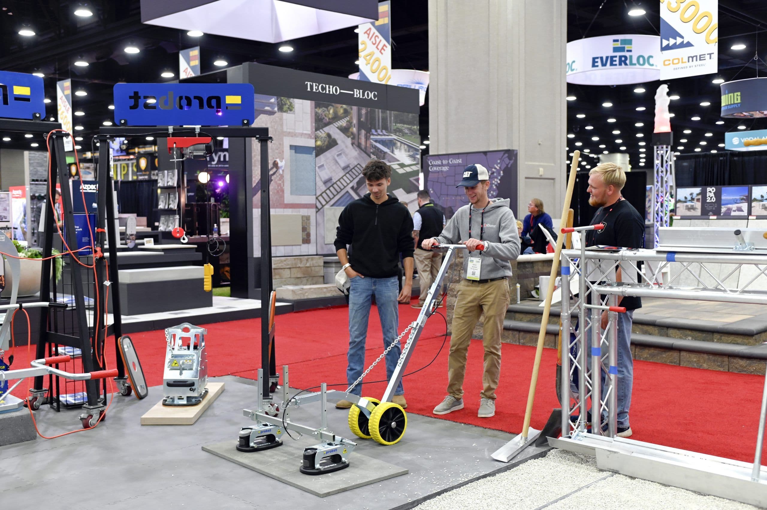 Three Hardscape North America attendees test hardscape installation equipment on the exhibition floor.