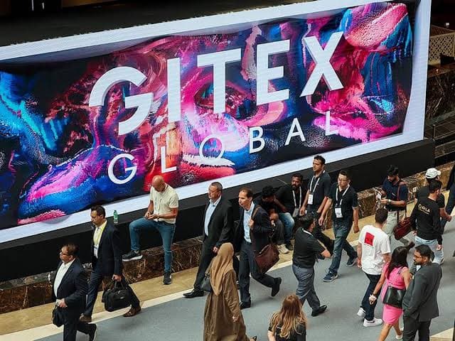Visitors walking past a large GITEX GLOBAL LED banner in the exhibition concourse