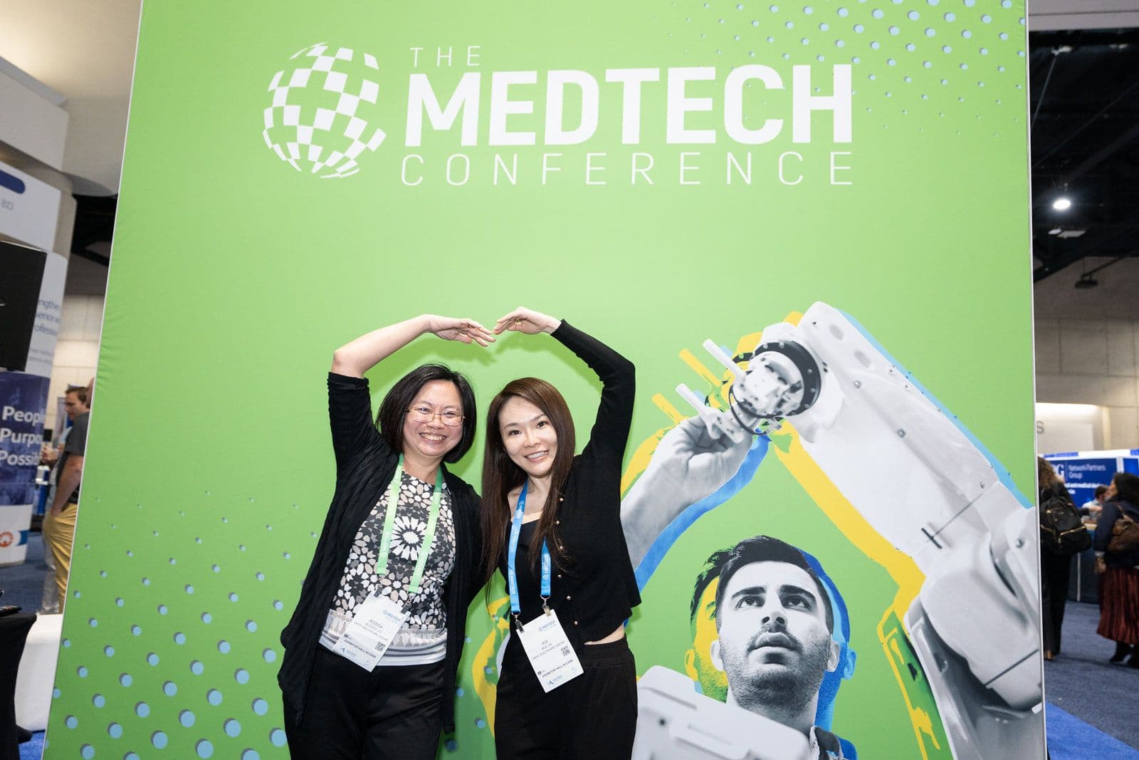 Two attendees at The MedTech Conference 2025 photo wall on the exhibit floor