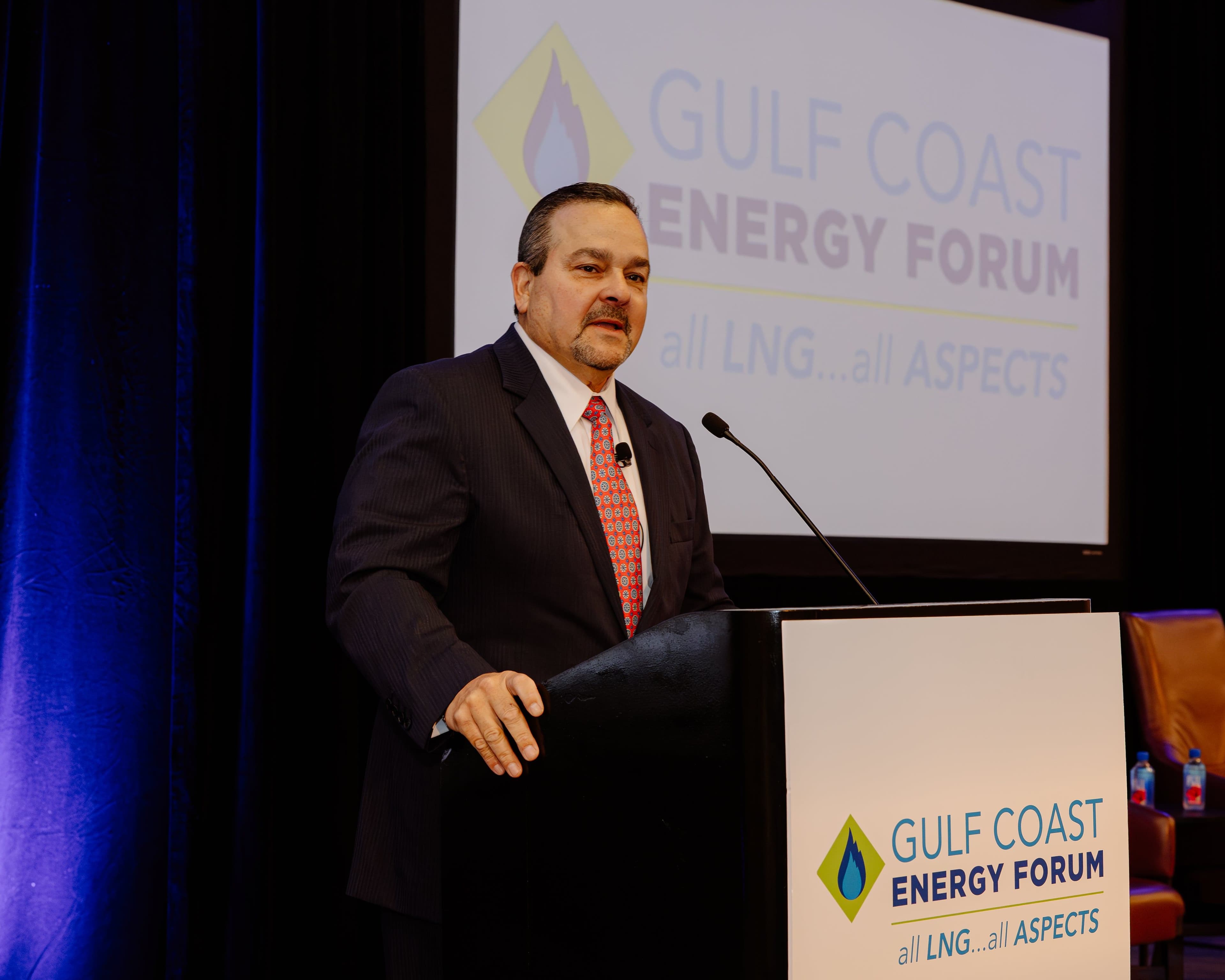 A speaker presents at the podium beneath the Gulf Coast Energy Forum 2025 logo screen in New Orleans.
