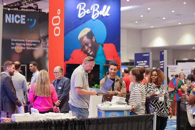 Attendees meeting with exhibitors at the NICE and 8x8 booths on the ICMI Contact Center Expo show floor