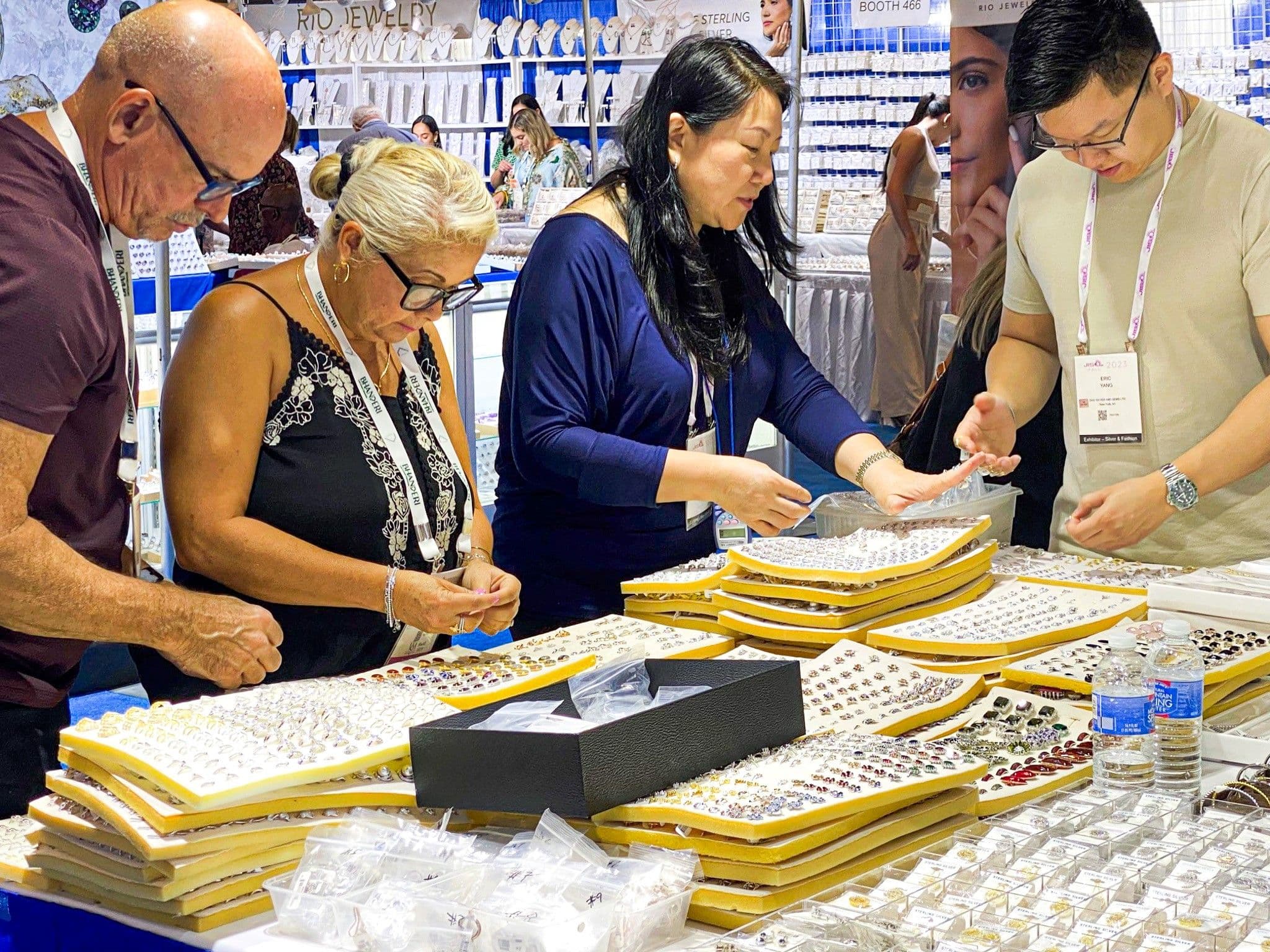 Retail buyers examining jewelry trays with an exhibitor on the JIS Fall 2023 show floor