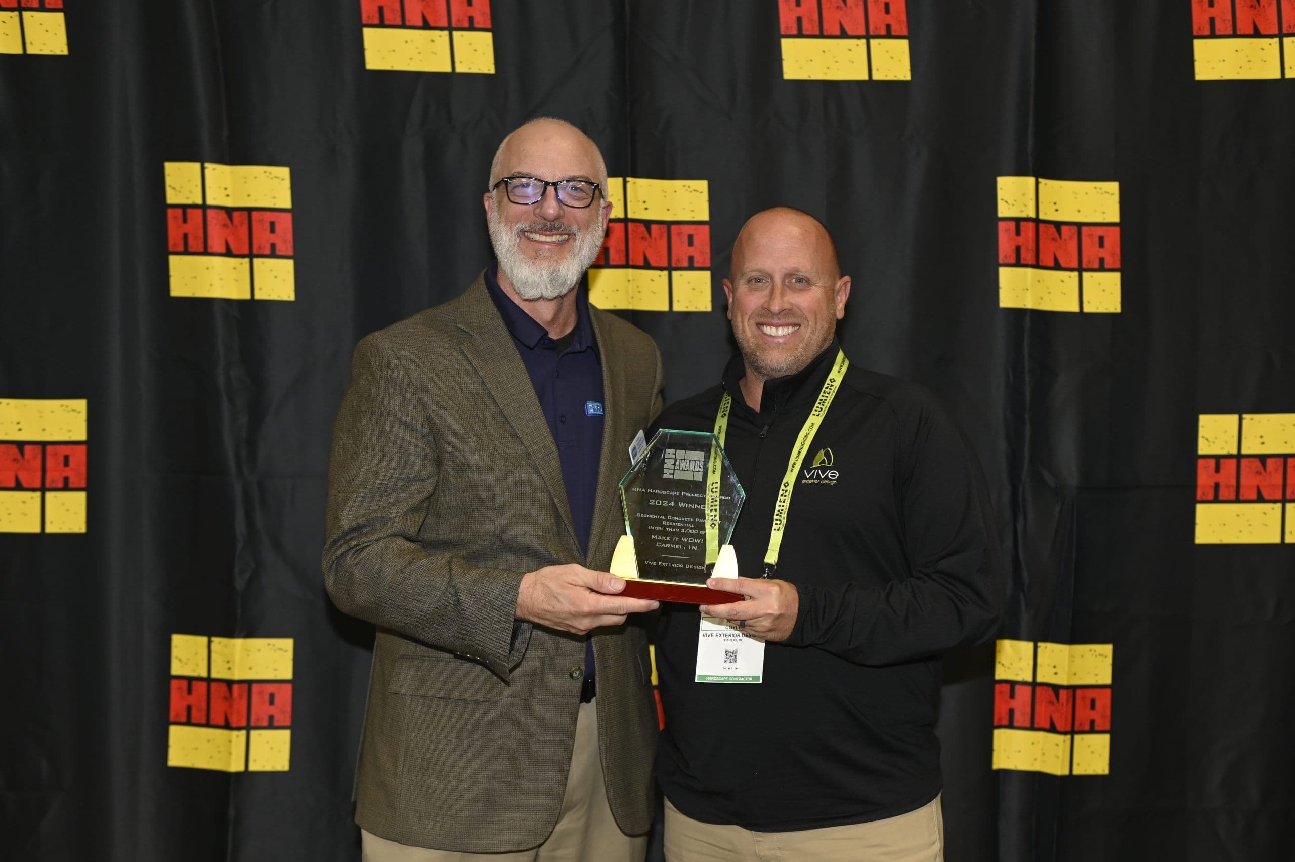 Two men hold a 2024 Hardscape North America award in front of an HNA backdrop.