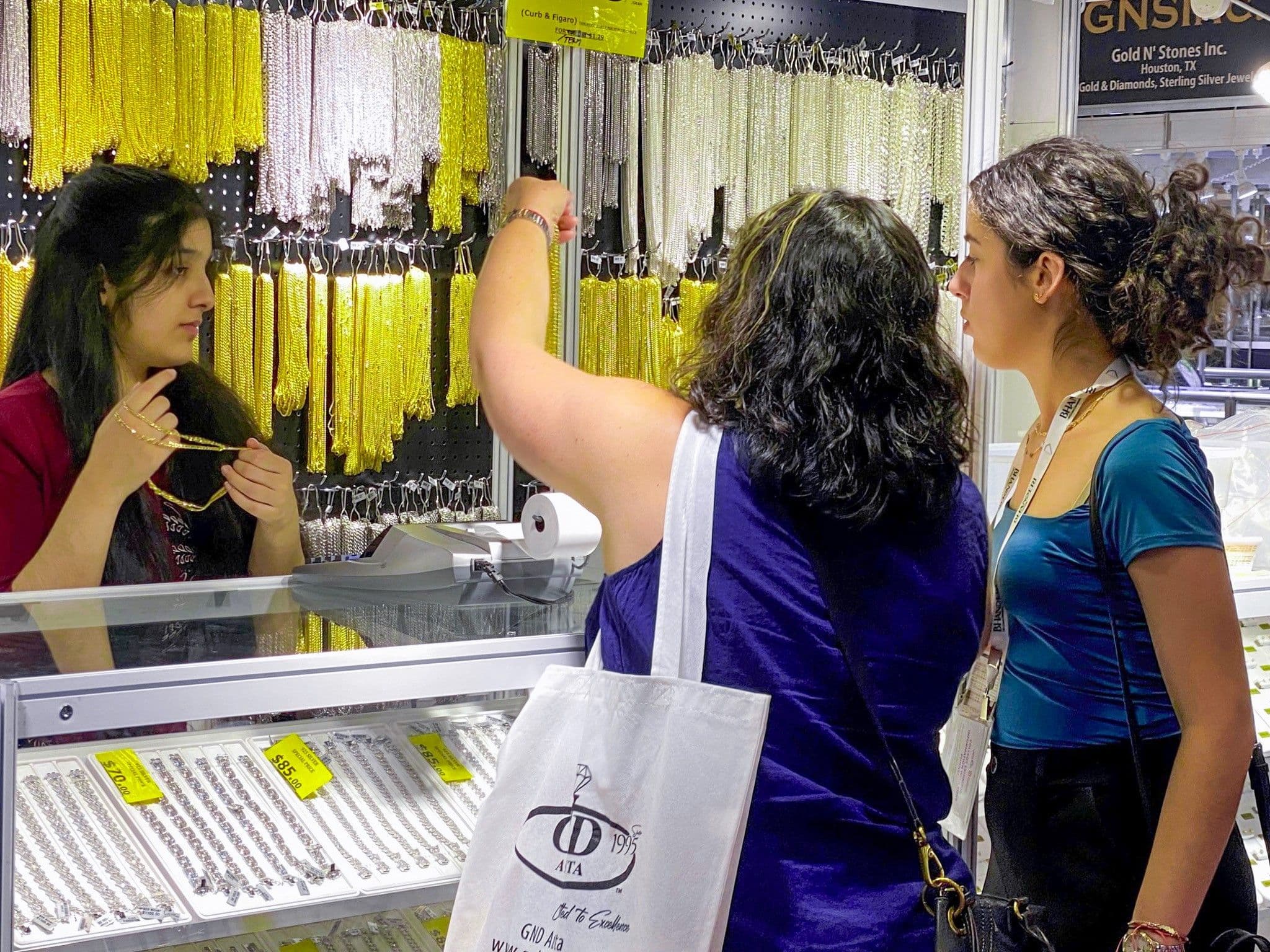 Attendees reviewing gold chains at an exhibitor booth during JIS Fall 2023