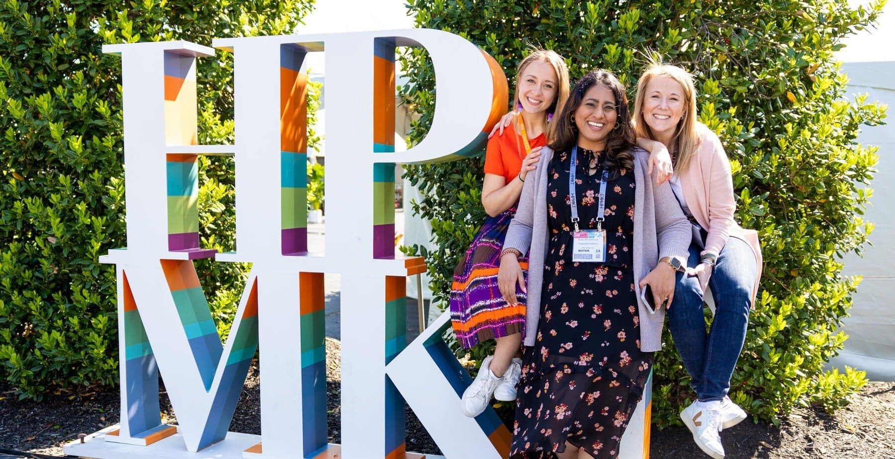 Three attendees pose beside the High Point Market sign during a prior market edition.